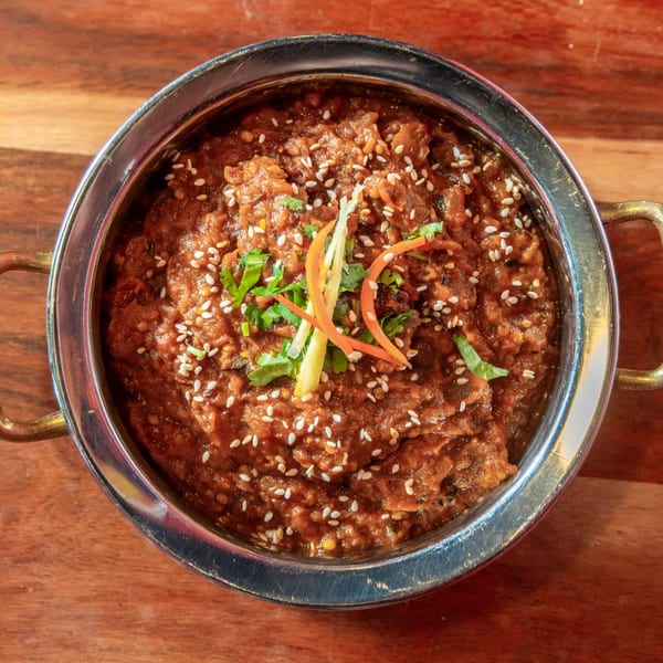 Indian curry in a metal bowl, garnished with sesame seeds, cilantro, and ginger strips.