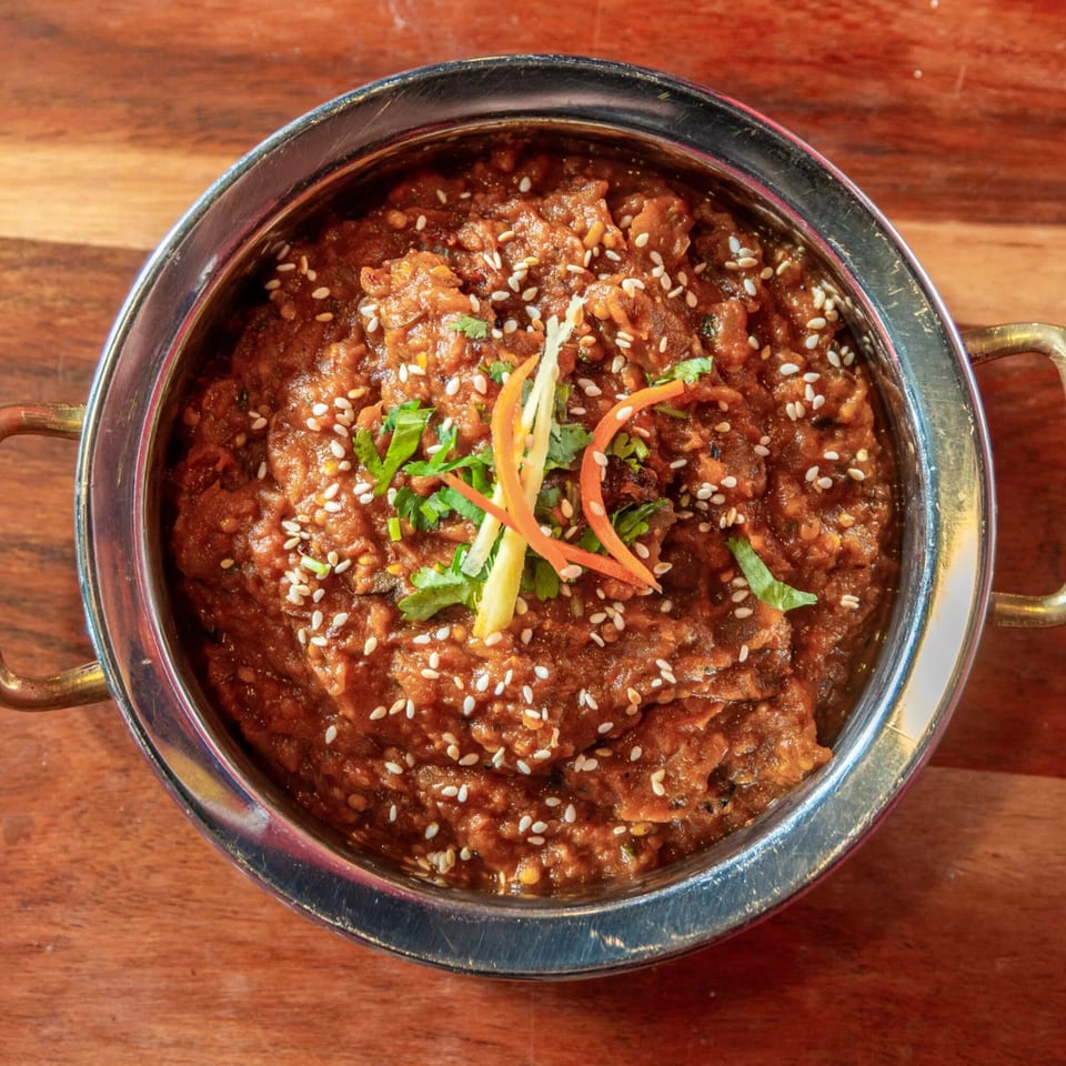 Indian curry in a metal bowl, garnished with sesame seeds, cilantro, and ginger strips.