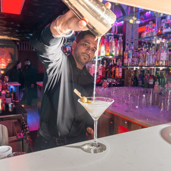 Bartender pouring a martini from a shaker into a glass with olives at Taste of Mumbai.