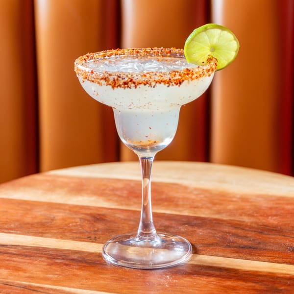A margarita with a chili-salt rim and lime wedge, on a wooden table at Taste of Mumbai.
