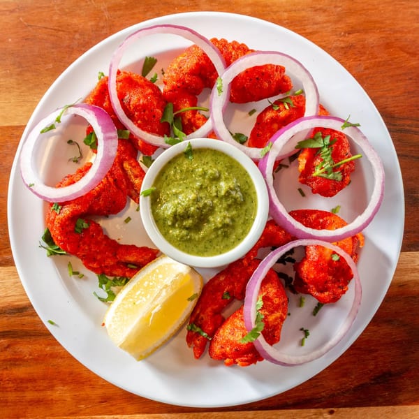 Bright red Indian chicken pakora with green chutney, red onion rings, and a lemon wedge.
