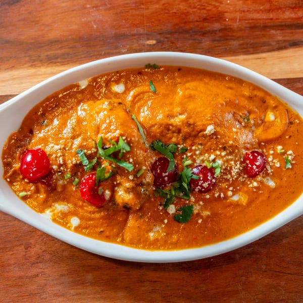 Indian butter chicken in a white bowl, garnished with cilantro, cheese, and red cherries.