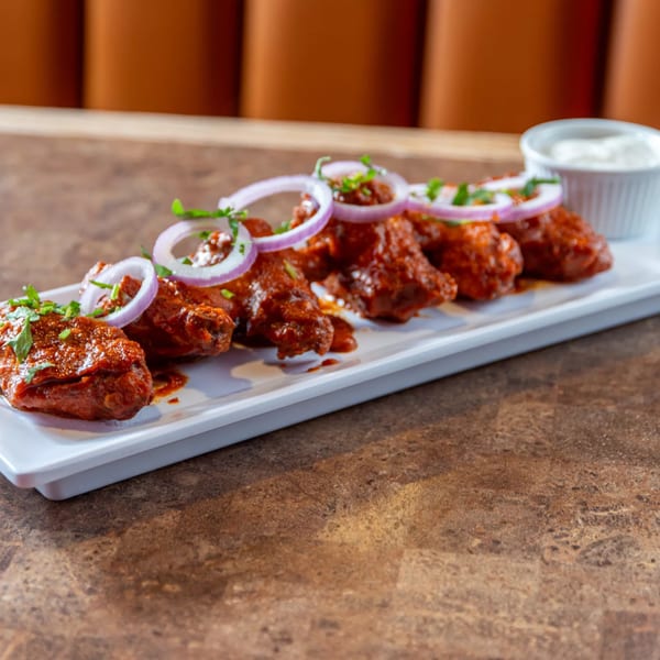 Spicy Indian chicken wings, garnished with red onion rings and fresh herbs, served with a white dipping sauce.