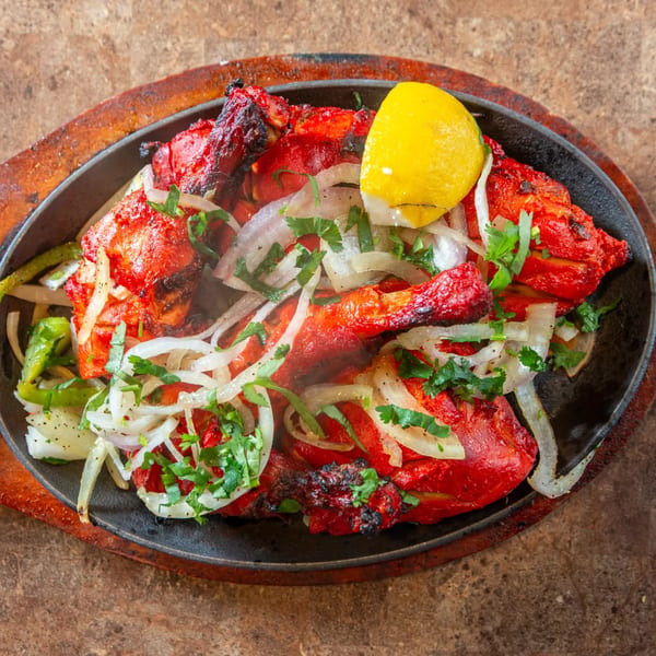 Sizzling Tandoori Chicken from Taste of Mumbai, garnished with onions, cilantro, and a lemon wedge.