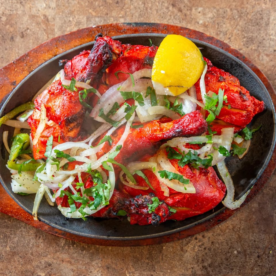 Sizzling Tandoori Chicken from Taste of Mumbai, garnished with onions, cilantro, and a lemon wedge.
