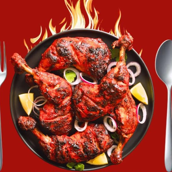 Taste of Mumbai's fiery tandoori chicken legs with onions and lemon wedges on a black plate.