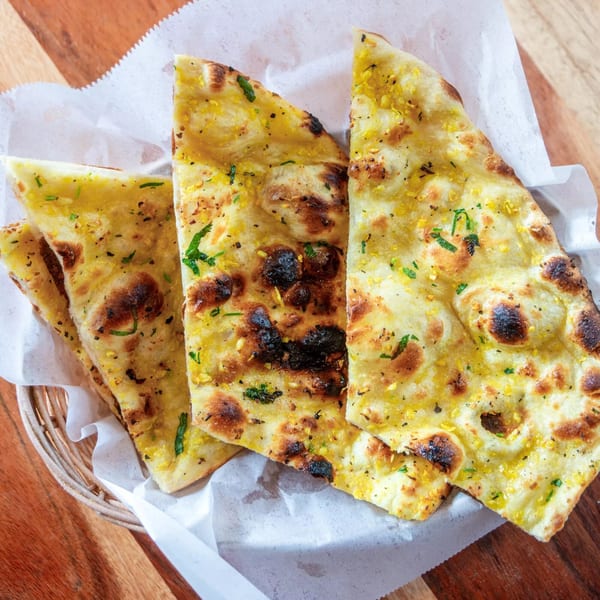 Golden garlic naan bread, garnished with herbs, served in a basket with white paper.