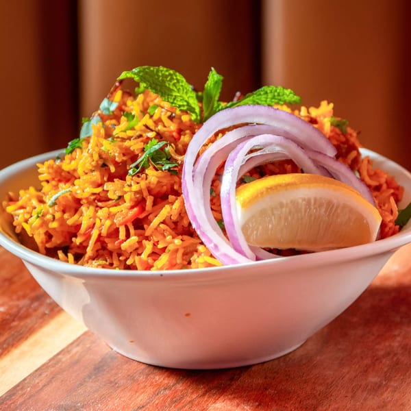 A white bowl of Indian biryani rice, garnished with red onion, mint, and a lemon wedge.