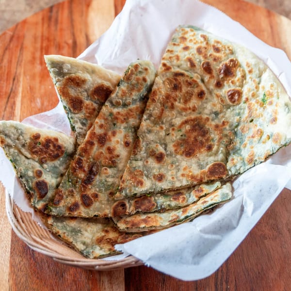 Basket of golden-brown Indian paratha flatbread, cut into triangles, on a wooden table.